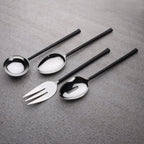 Set of black-handled cutlery including a fork, spoon, and ladle on a gray surface.