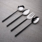 Set of black-handled silverware including spoons and a fork on a gray surface