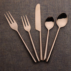 Set of rose gold cutlery including forks, knife, and spoons on a brown textured background