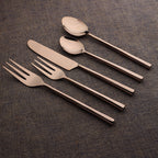 Set of silver cutlery including knife, fork, and spoons on a brown textured surface.