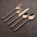 Set of bronze cutlery including knives, forks, and spoons on a textured brown surface.