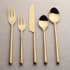 Set of gold cutlery including a knife, two forks, and two spoons on a textured gray background.