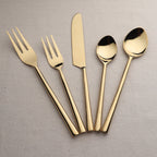 Set of gold cutlery including fork, knife, and spoons on a gray background