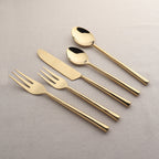 Set of gold cutlery including knife, fork, and spoons on a light gray background