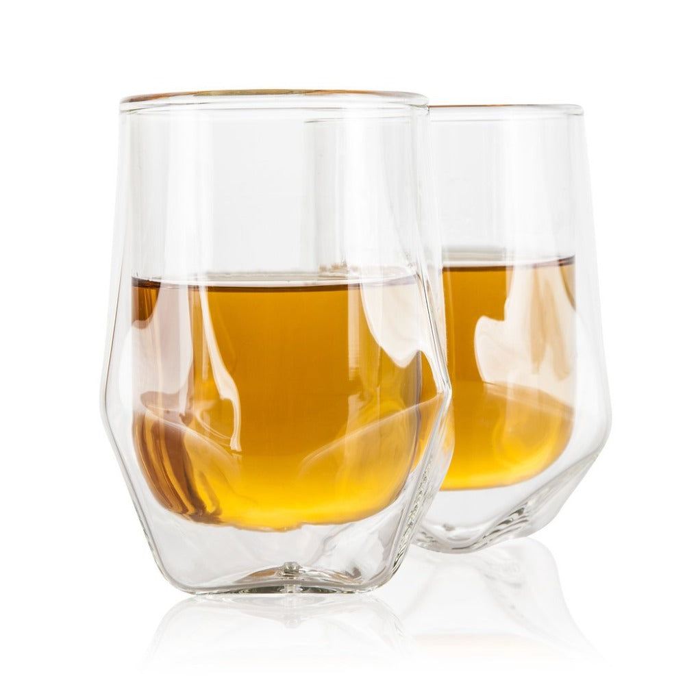 Two clear glass tumblers filled with a amber liquid on a white background