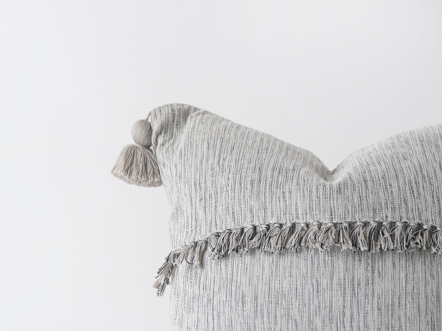 Textured gray pillow with tassels on a light gray background