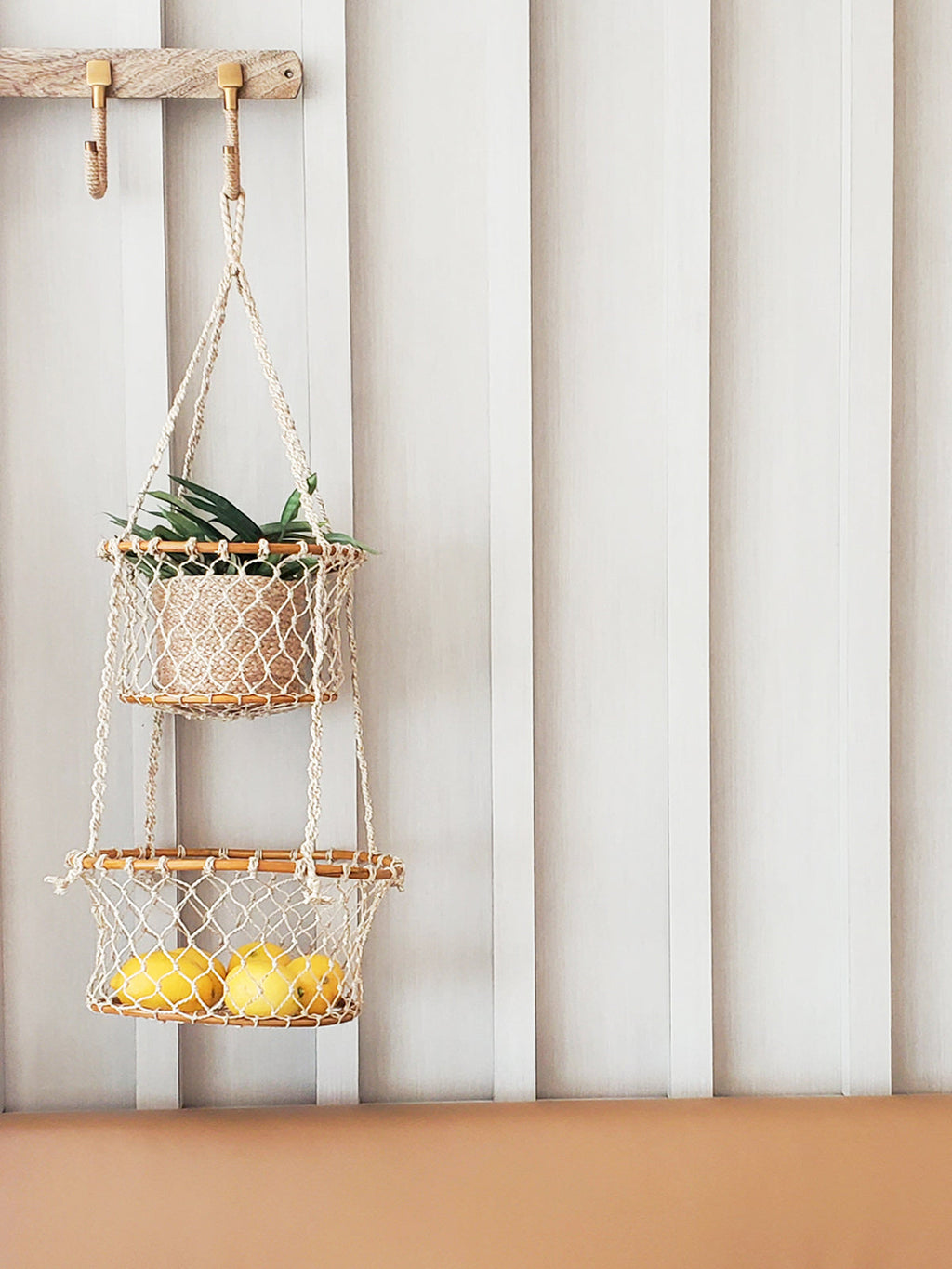 Two-tiered macrame plant hanger with a plant and lemons against a striped wall.