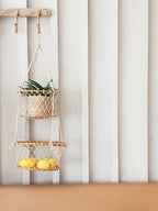 Two-tiered macrame plant hanger with a plant and lemons against a striped wall.