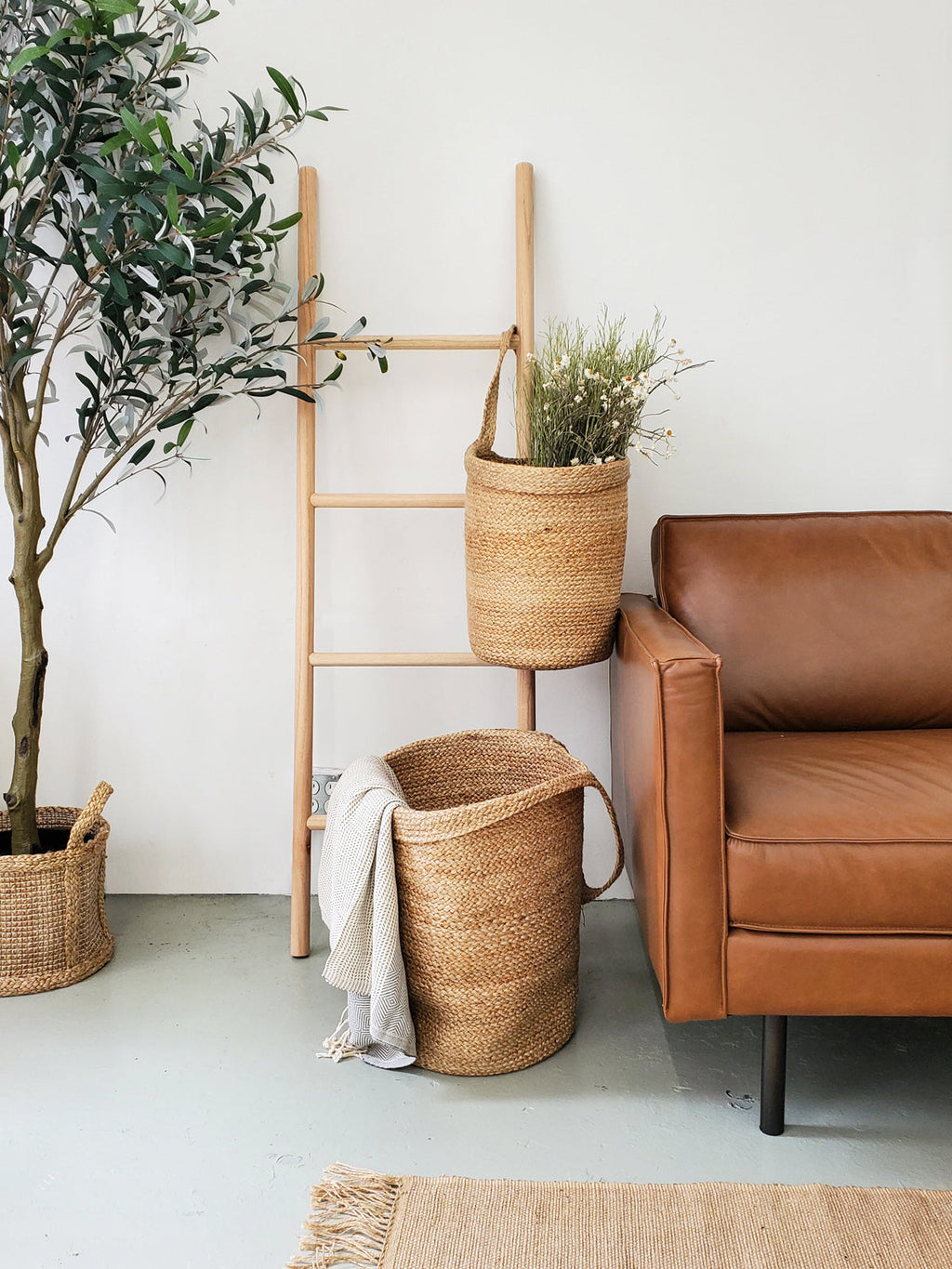 Living room with brown leather sofa, wicker baskets, and a ladder against a white wall.