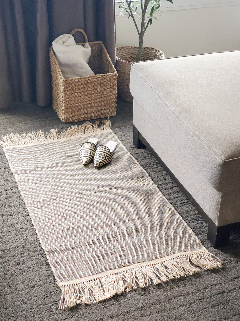 Gray rug with tassels on a carpeted floor in a living room setting.