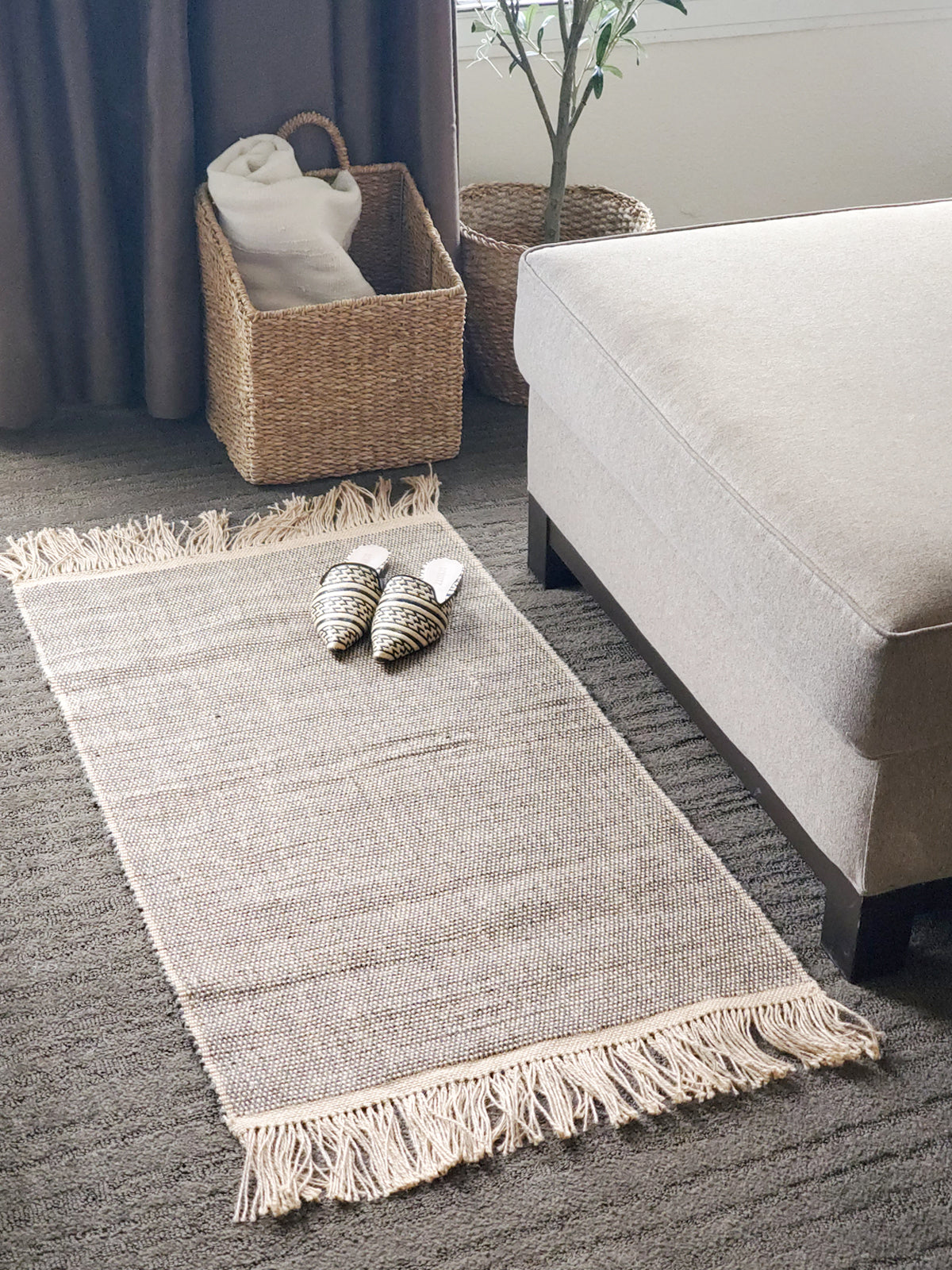 Gray rug with tassels on a carpeted floor in a living room setting.