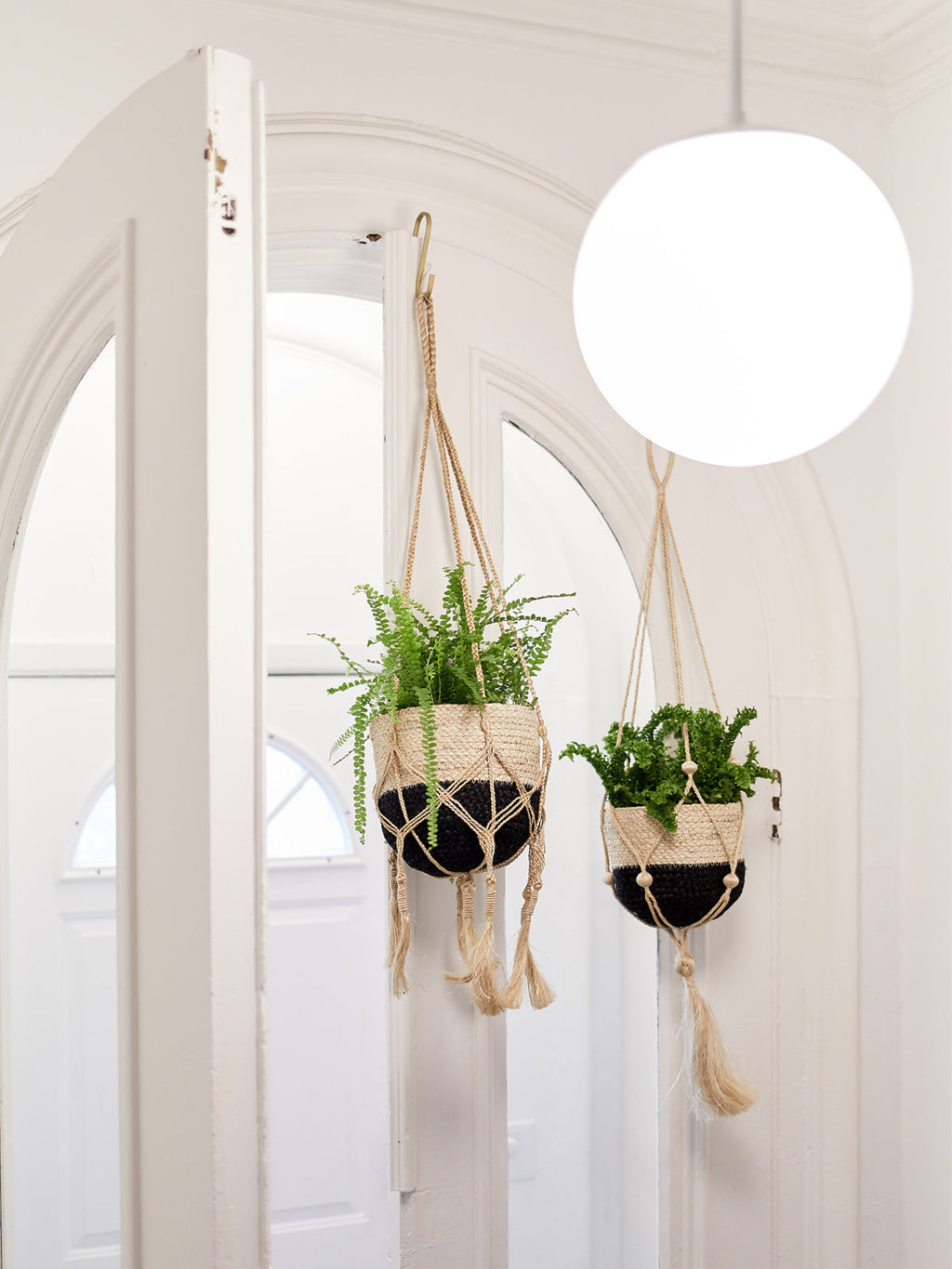 Two hanging planters with green plants against a white wall.