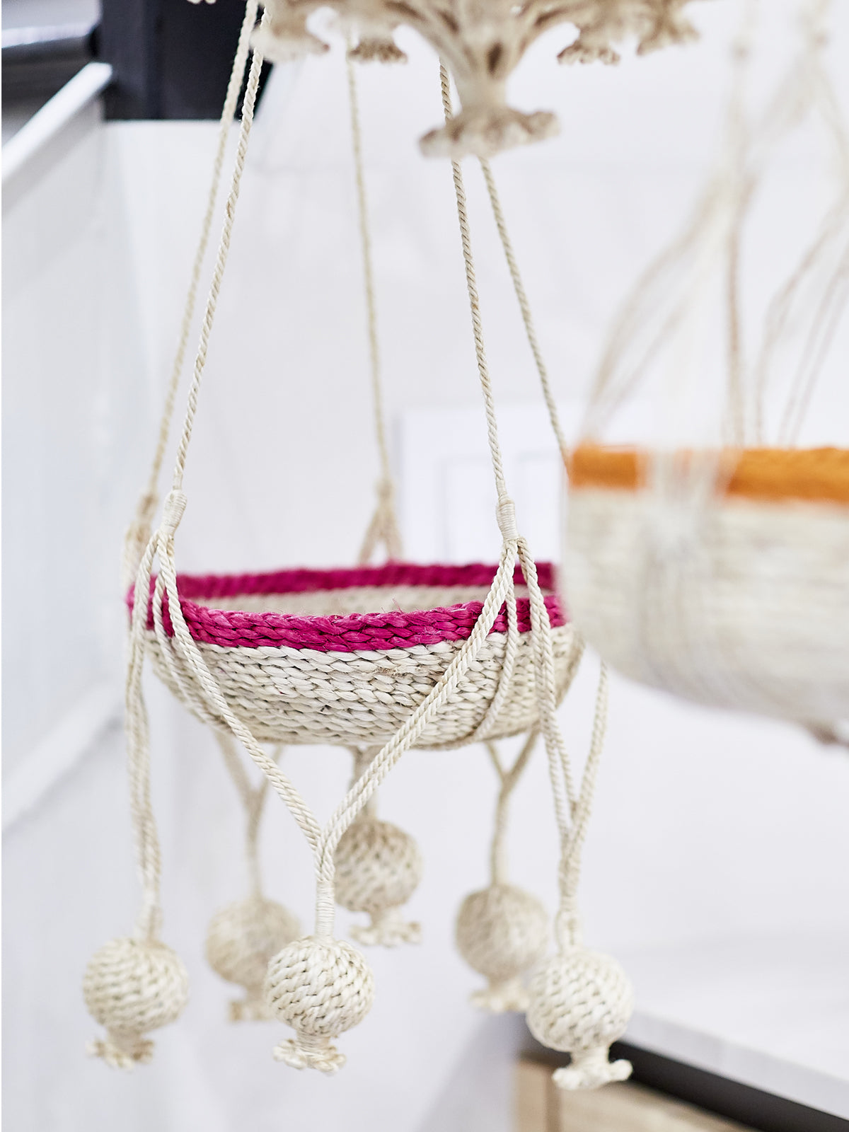 Macrame plant hanger with pink woven basket on a white surface