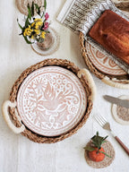 Decorative ceramic plate with floral design in a woven basket on a table with bread and flowers.