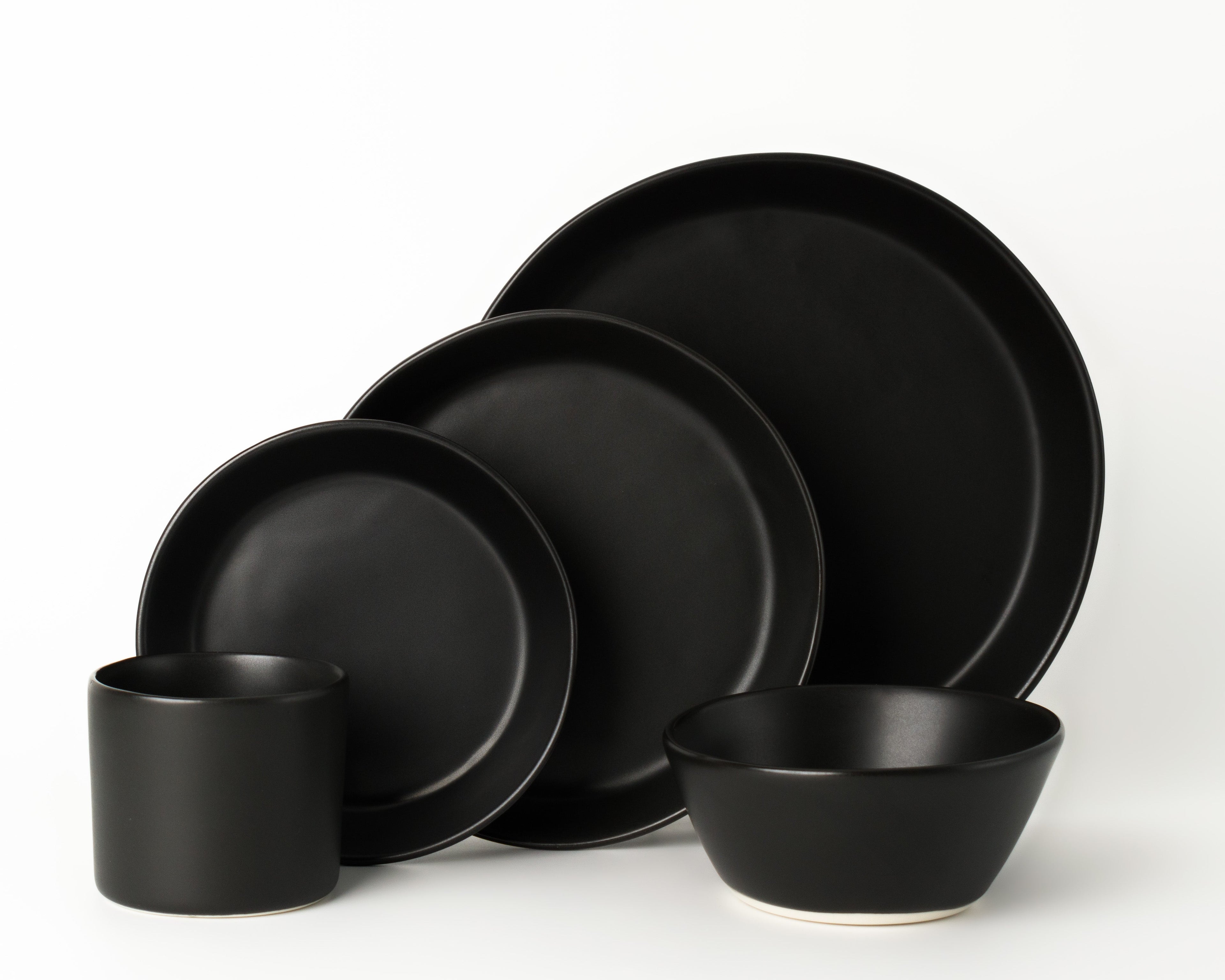 Set of black ceramic dinnerware including plates and bowls on a white background