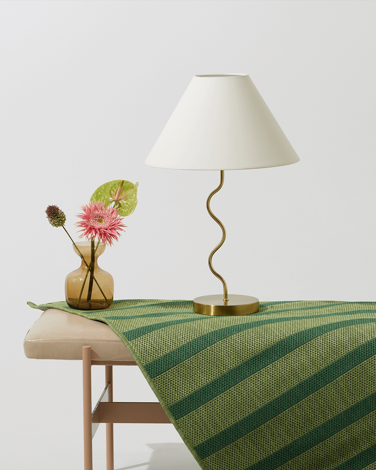 Table with a green and yellow striped tablecloth, vase with flowers, and lamp on a light gray background