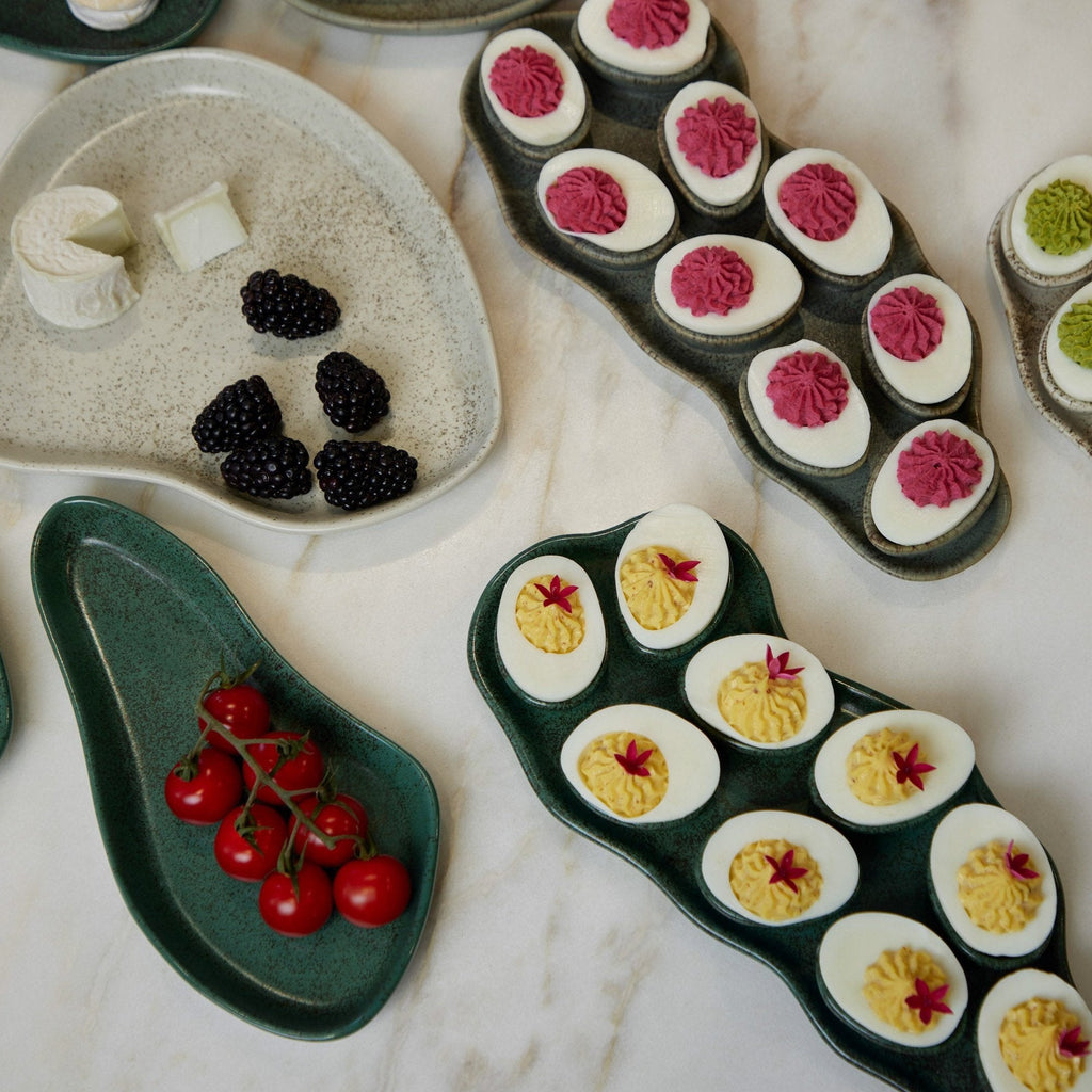 Assorted deviled eggs and blackberries on ceramic trays.