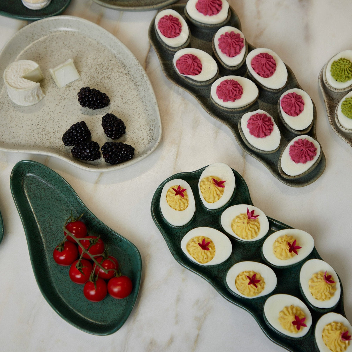 Assorted deviled eggs and blackberries on ceramic trays.