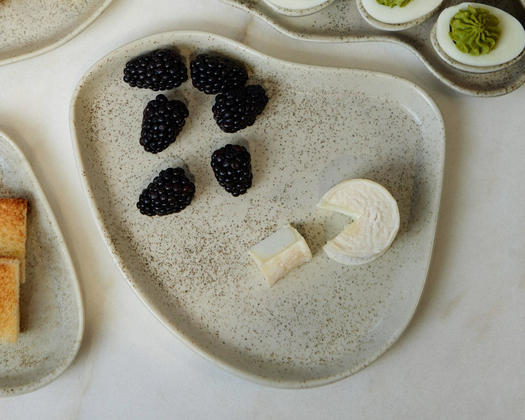 Heart-shaped ceramic plate with blackberries, cream cheese, and deviled eggs on a marble surface.