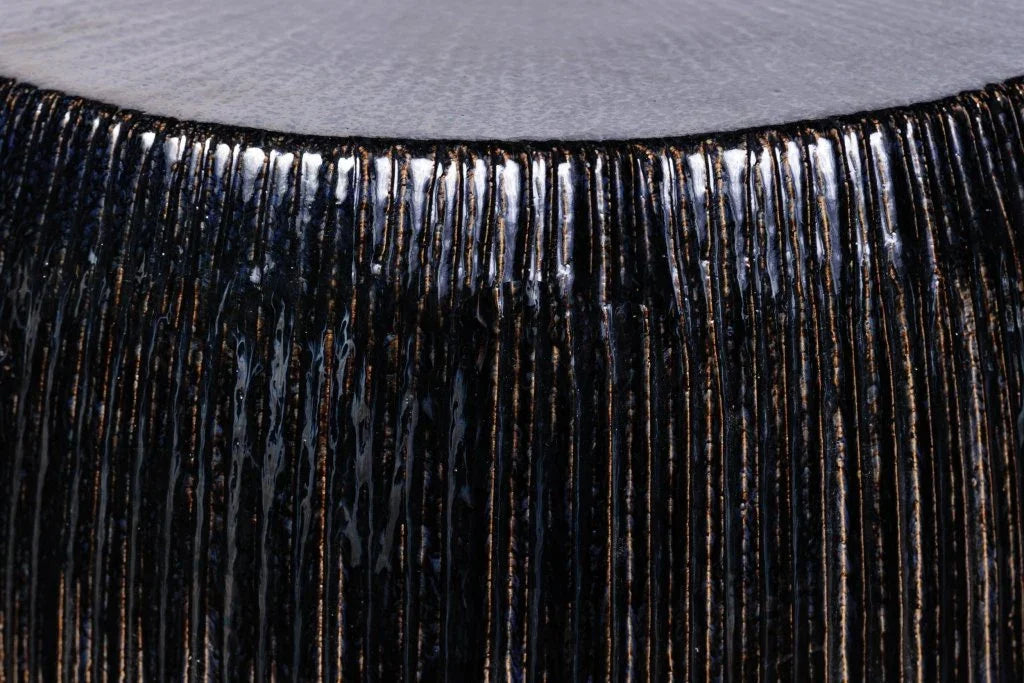 Close-up of black fringe on a textured stool surface