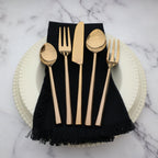 Gold cutlery set on a black napkin with white plates on a marble surface