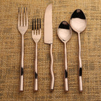 Set of copper cutlery with black accents on a textured beige background
