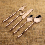 Set of rose gold cutlery including fork, knife, and two spoons on a textured brown background.