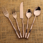 Set of rose gold cutlery including a fork, knife, and two spoons on a textured brown background.