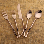 Set of bronze cutlery including forks and knives on a textured beige background