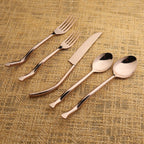 Set of rose gold cutlery including fork, knife, and two spoons on a textured beige background.