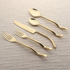 Set of gold cutlery including knife, fork, and spoons on a textured beige surface.
