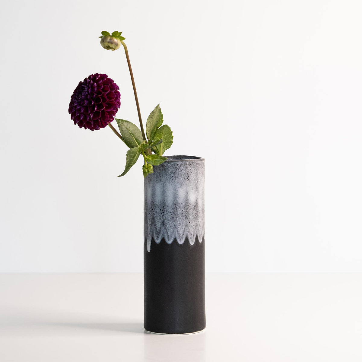Black and white textured vase with a single purple flower on a white background