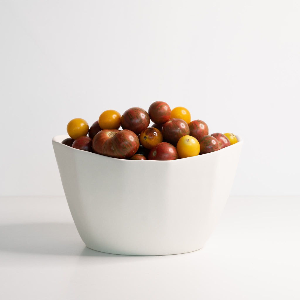 White bowl filled with multicolored tomatoes on a light gray background