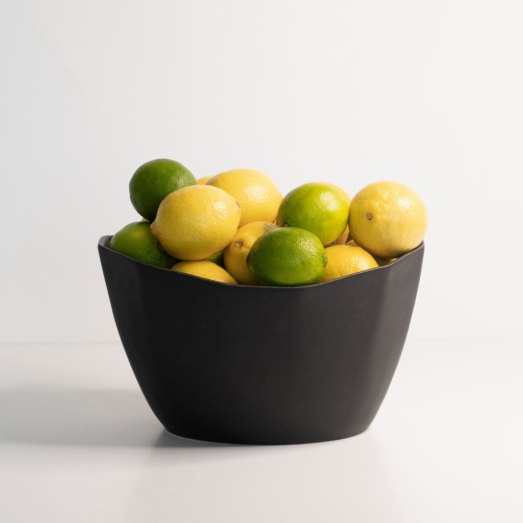 Black bowl filled with lemons and limes on a white background