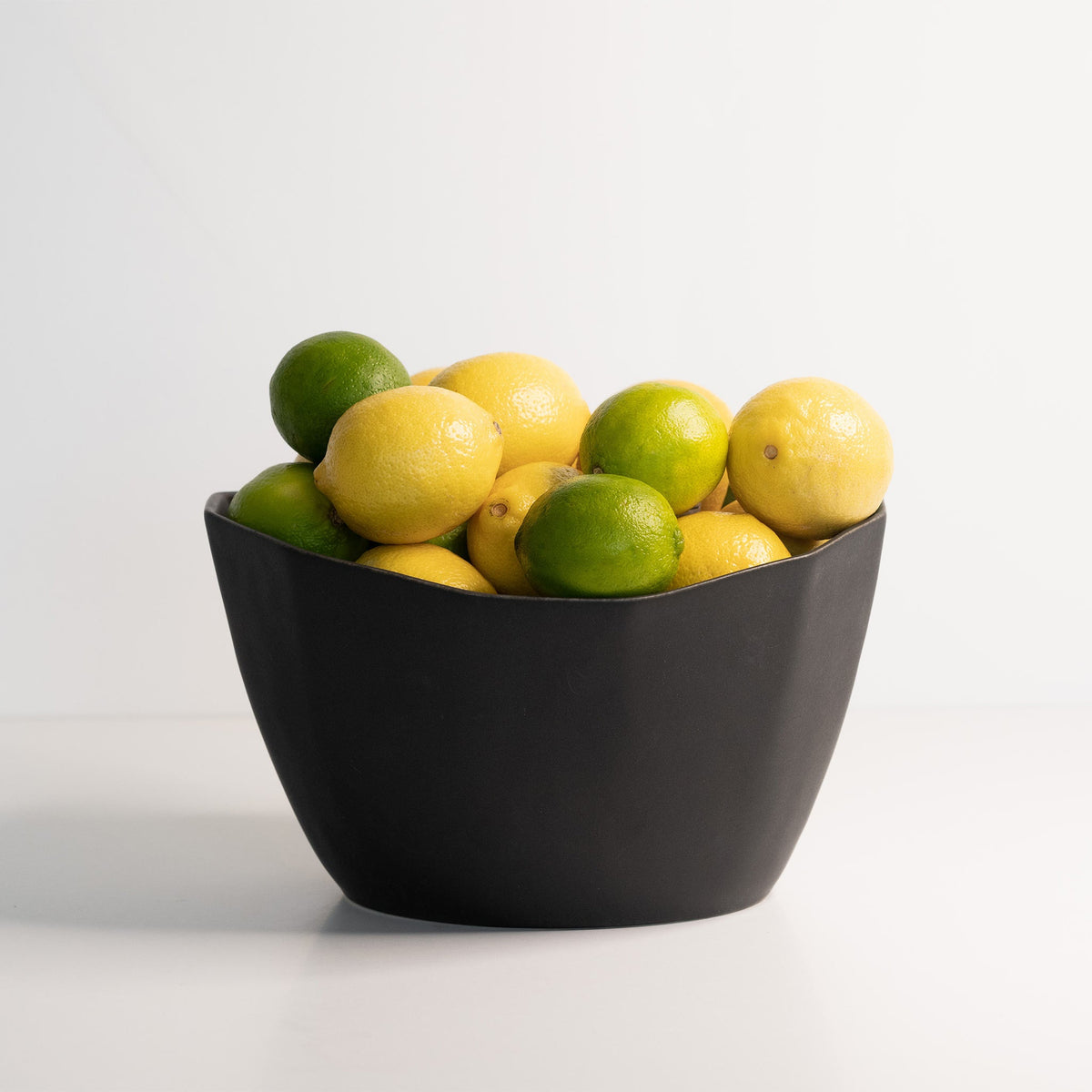 Black bowl filled with lemons and limes on a white background