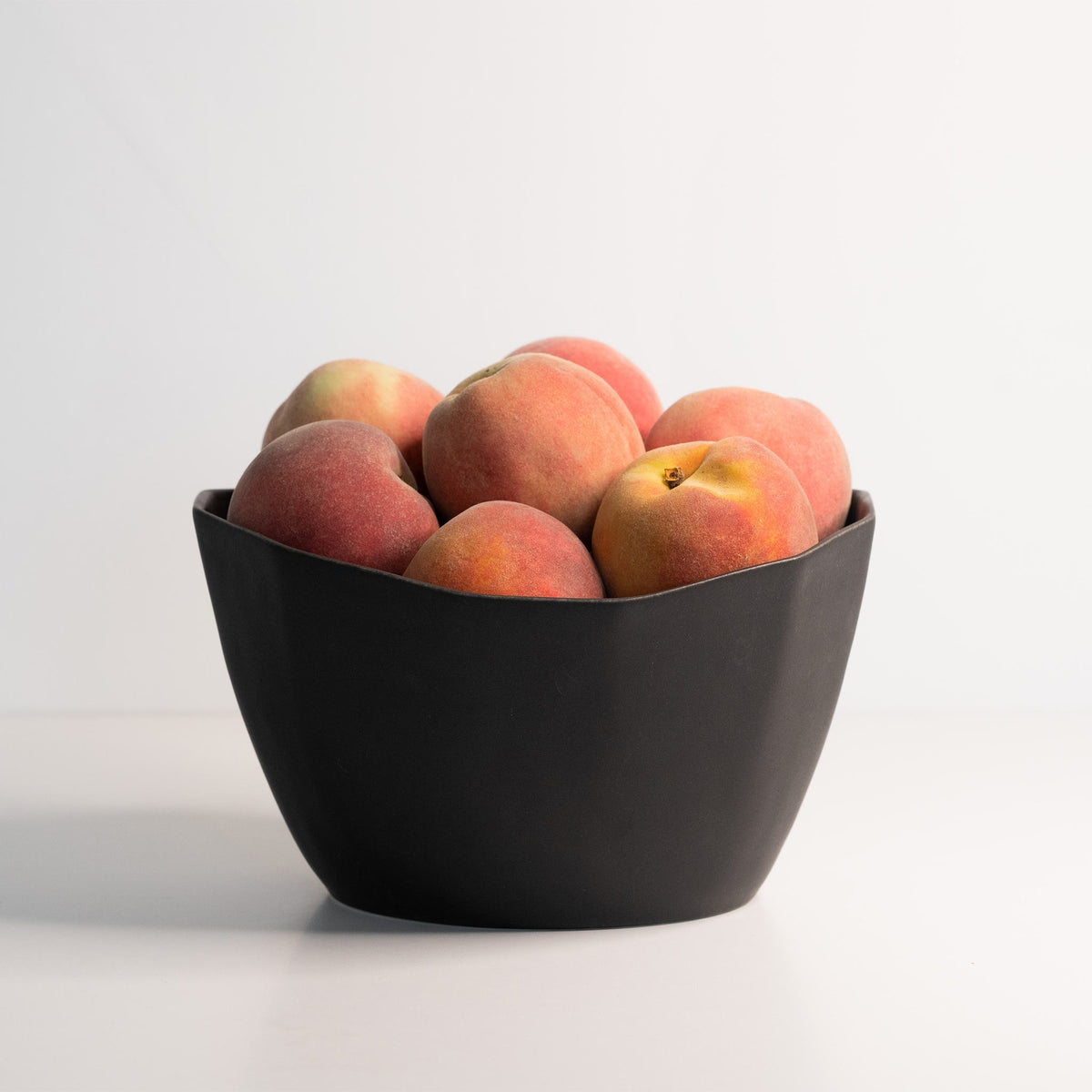 Black bowl filled with peaches on a white background
