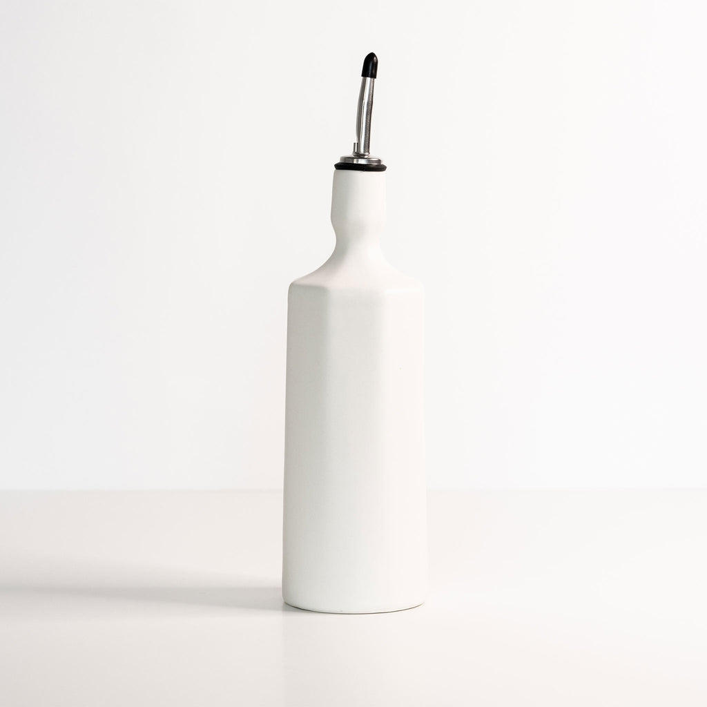 White ceramic olive oil bottle with a black lid on a white background