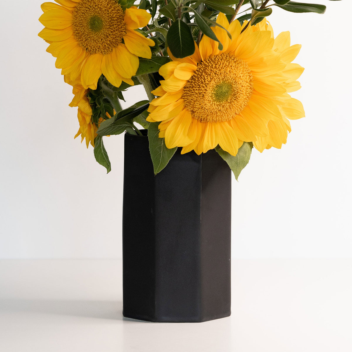 Yellow sunflowers in a black vase on a white background