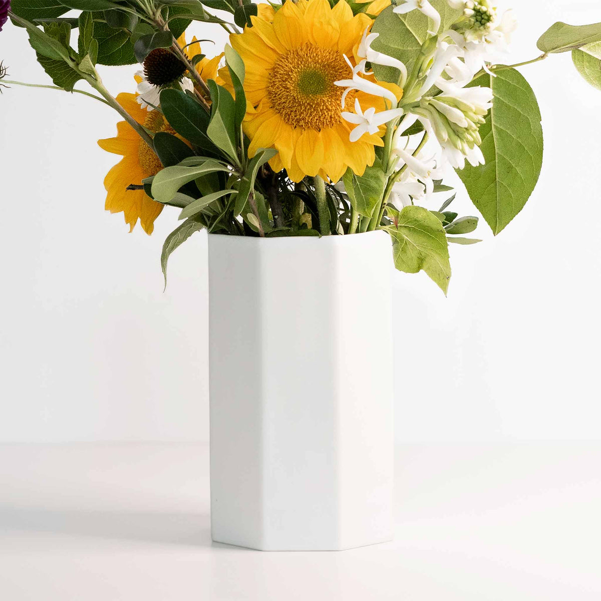 White vase with sunflowers and greenery on a light background