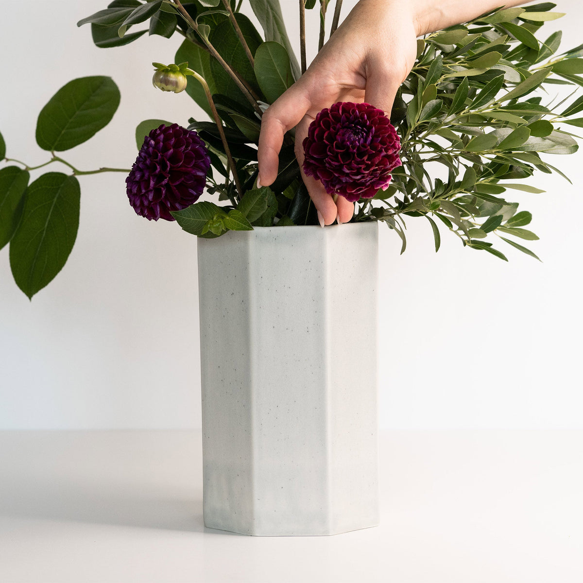 Person arranging flowers in a white hexagonal vase on a light background