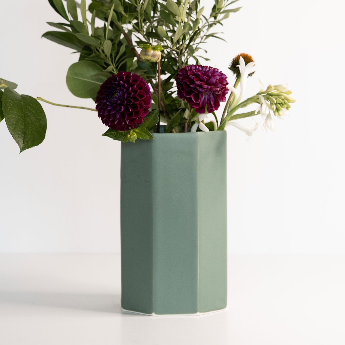 Green vase with purple flowers on a white background