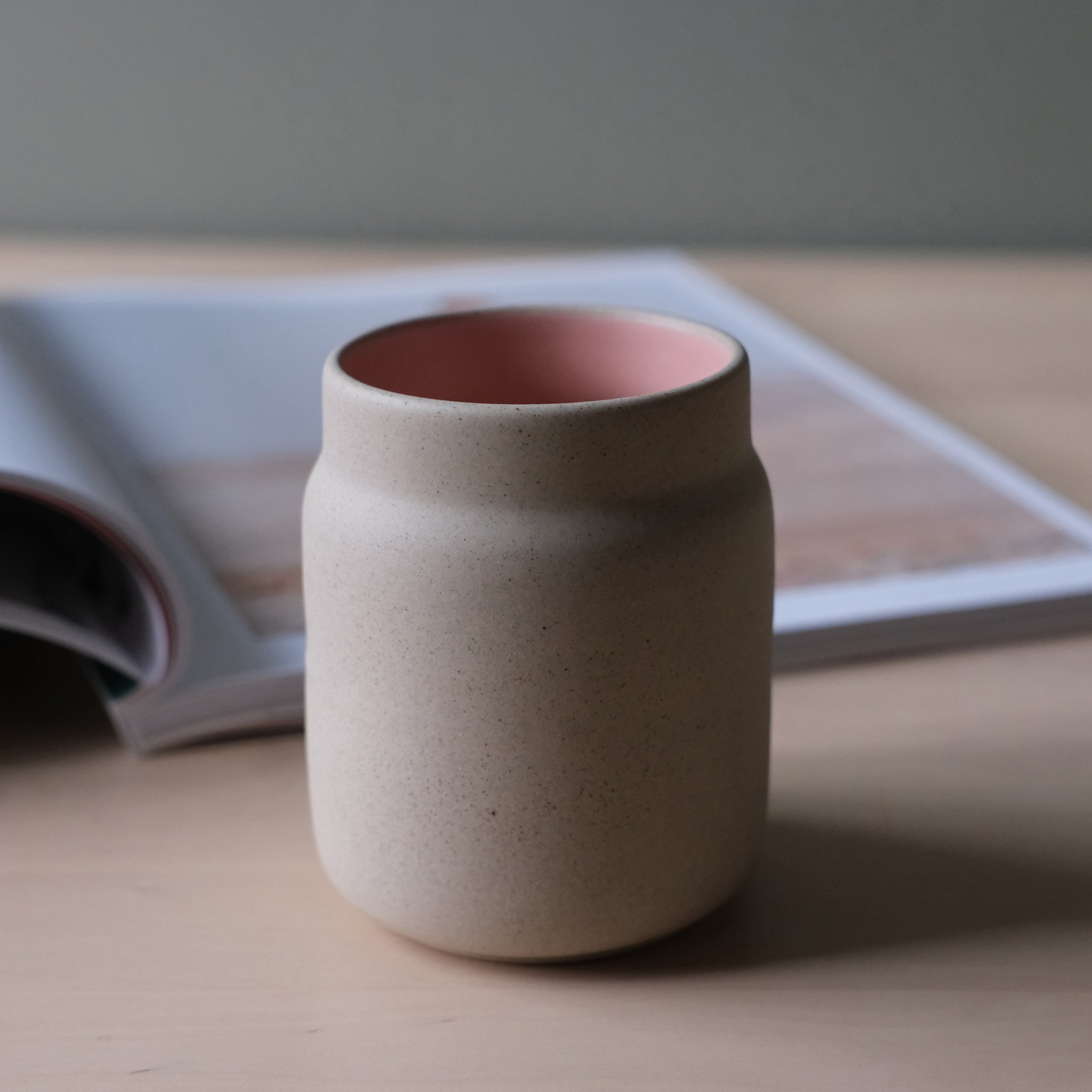 Ceramic cup with pink interior on a wooden surface with an open book in the background