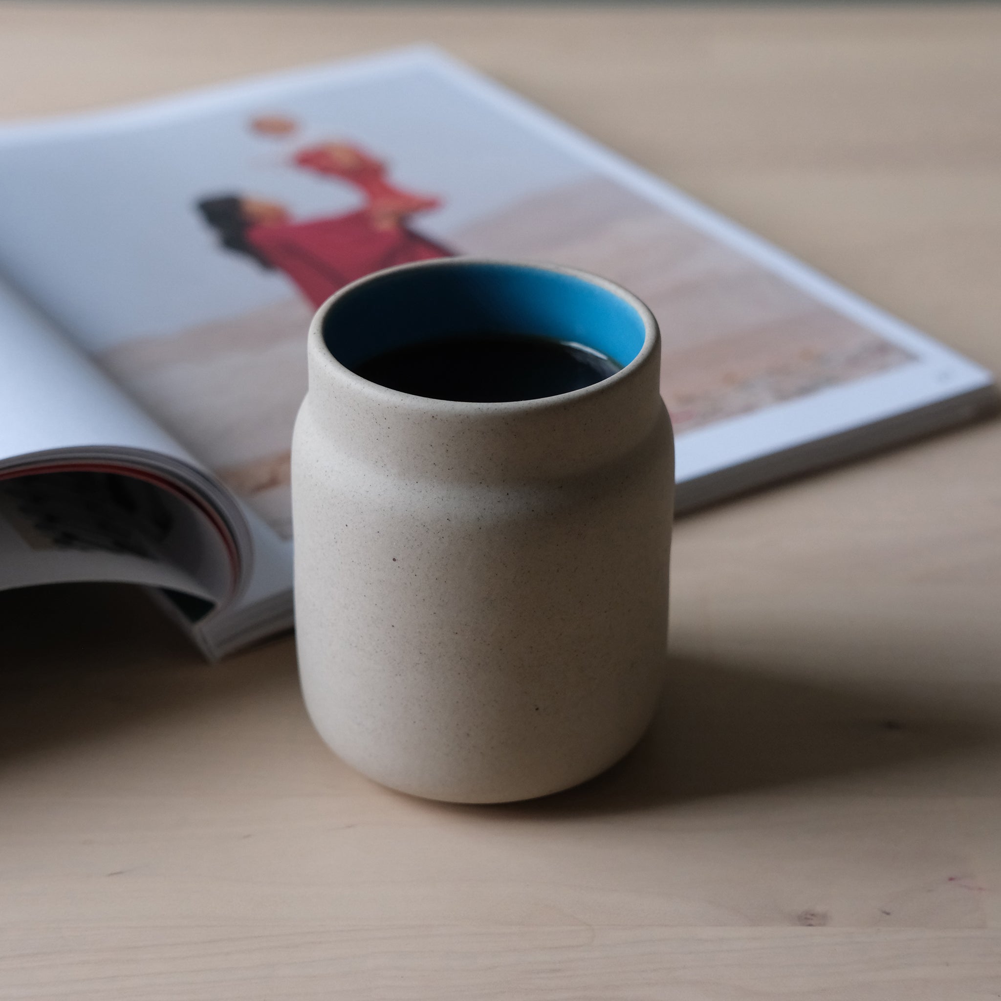 Ceramic cup with blue interior on a wooden surface next to an open book