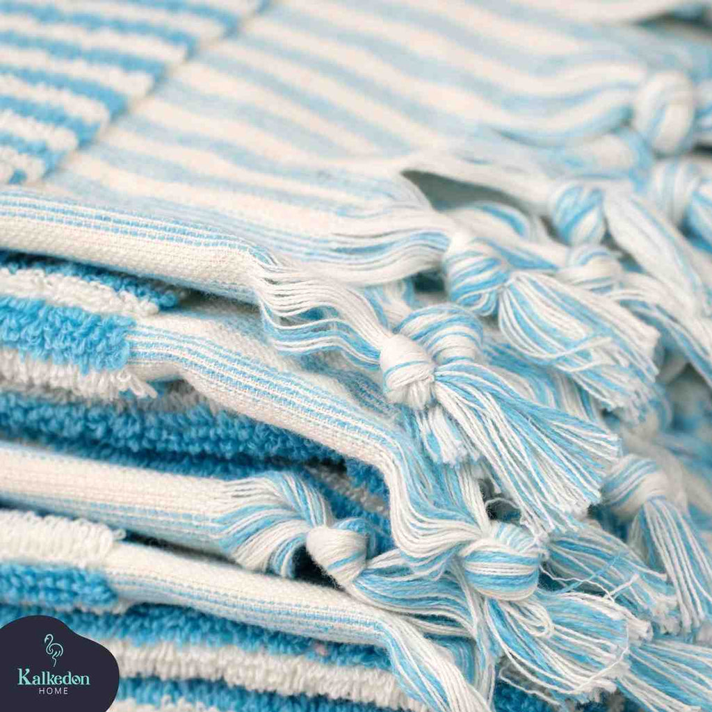 Stack of turquoise and white striped hand towels with knotted fringe detail