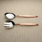 Two salad servers with copper handles on a textured beige surface