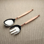 Set of salad servers with copper handles on a textured surface