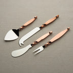 Set of four metal cheese tools with rose gold handles on a gray background