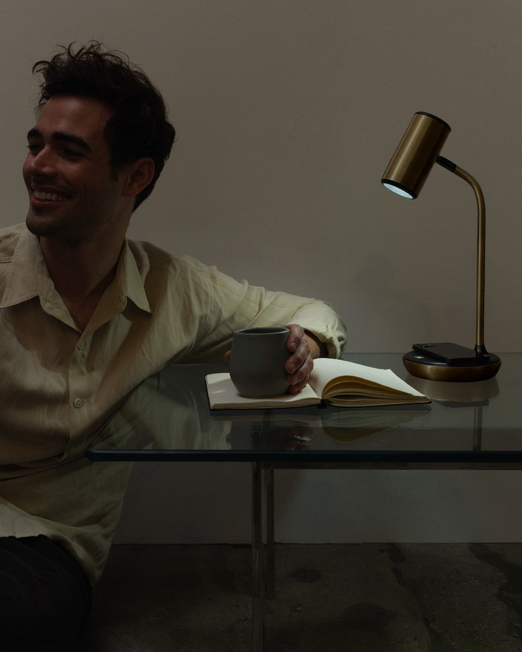 Man sitting at a table with a lamp and book, smiling.