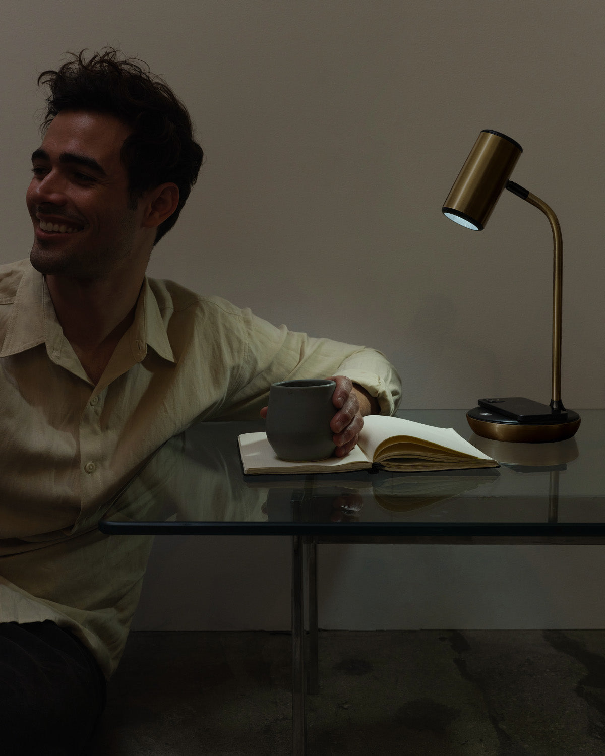 Man sitting at a table with a lamp and book, smiling.