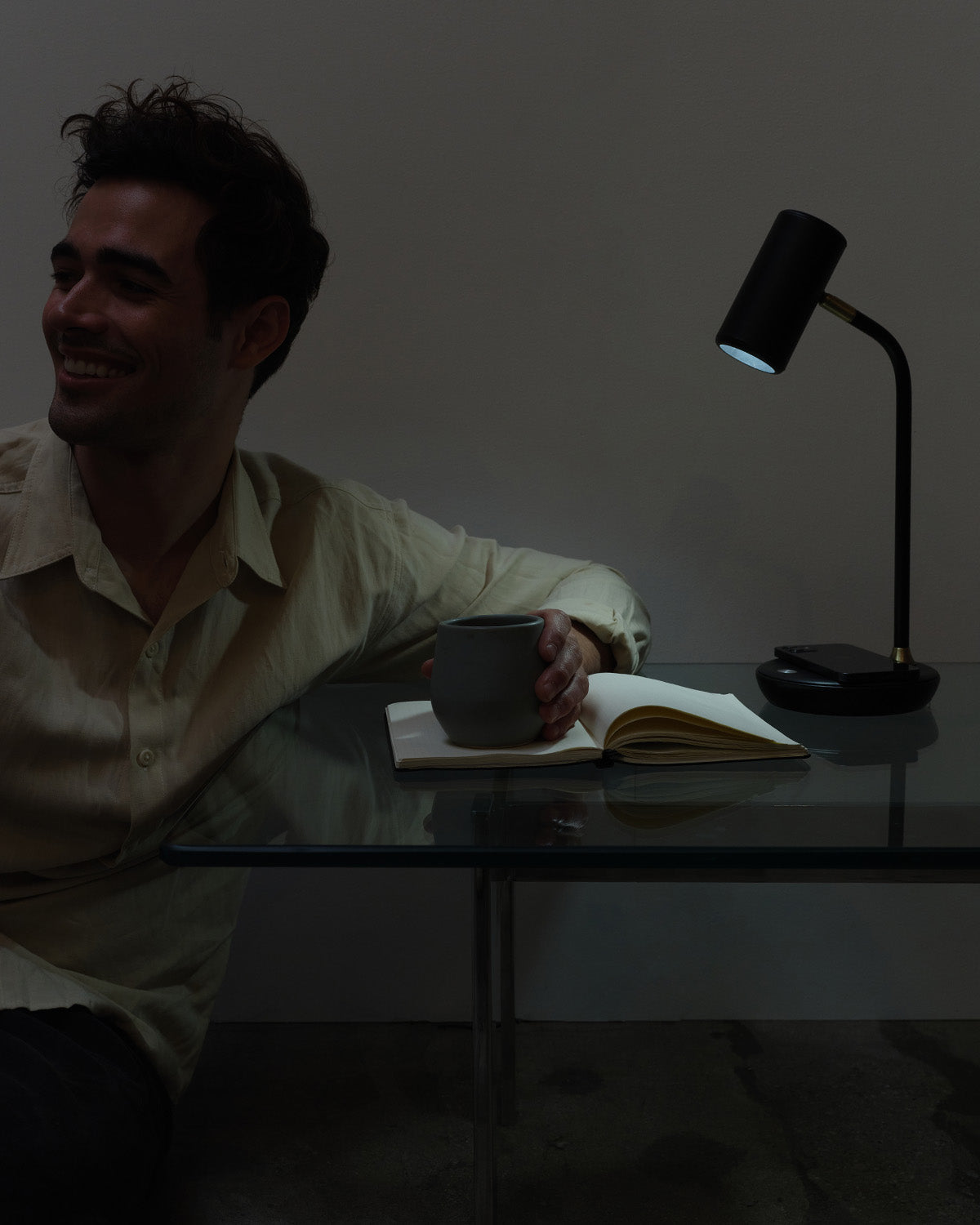 Man sitting at a desk with a lamp and notebook in a dimly lit room